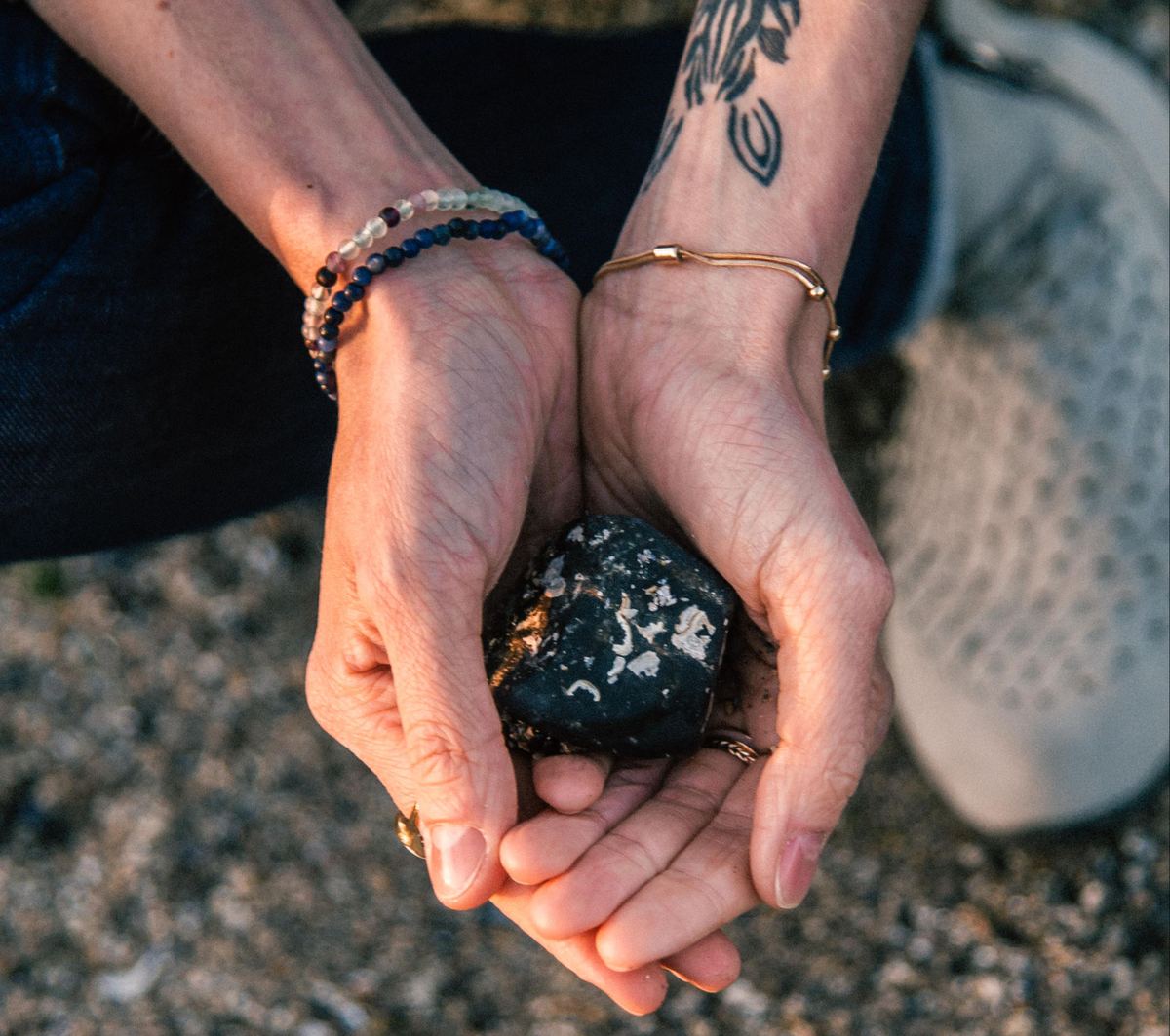 Two hands cupped together on a pebble beach, holding a dark stone